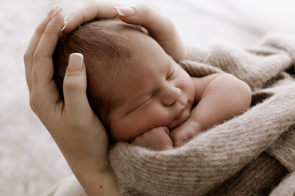 sleeping baby, cradled by mums hands, content and snuggly dreaming with hand under cheek.